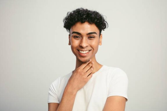 Portrait of a handsome gay man on white background. Smiling young man with cool hairstyle looking at camera.