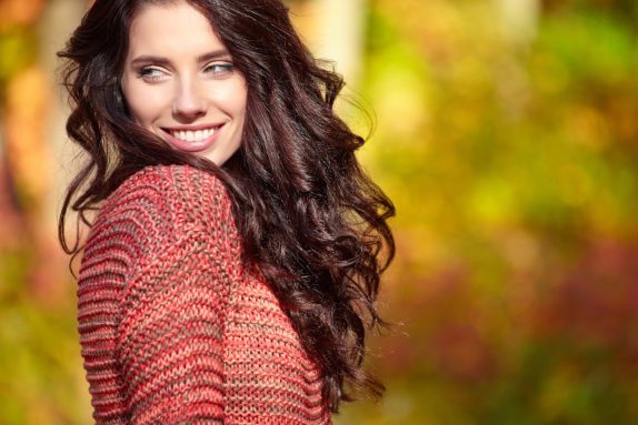 a smiling woman outside in fall, showing what a patient would look like after a pick me up procedure like a mini facelift, eyebrow lift, or botox